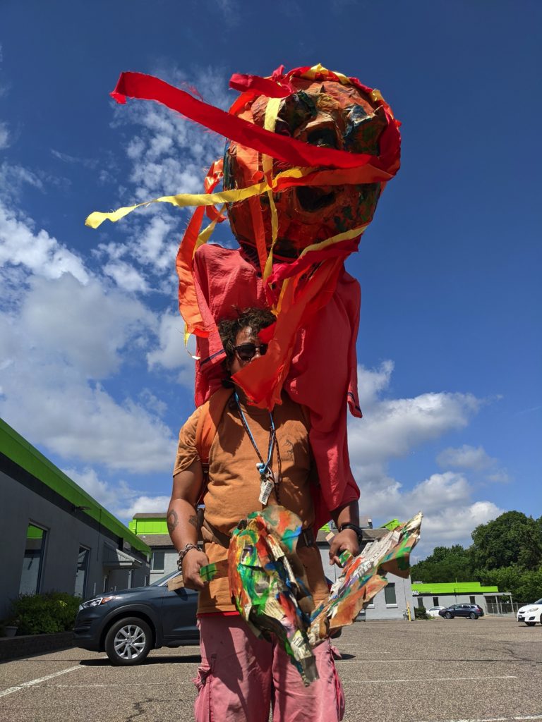 A person carries a huge multi-colored puppet on his shoulders
