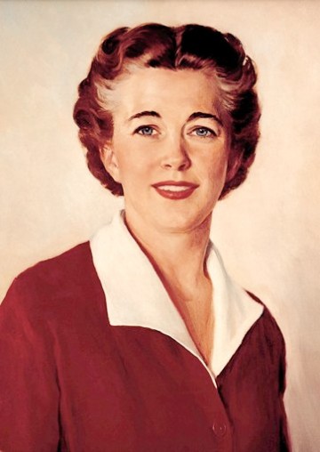 An image of the 1955 version of Betty Crocker: a woman in a dark red suit with wide white collars; a hint of gray in her dark hair, and red lipstick.