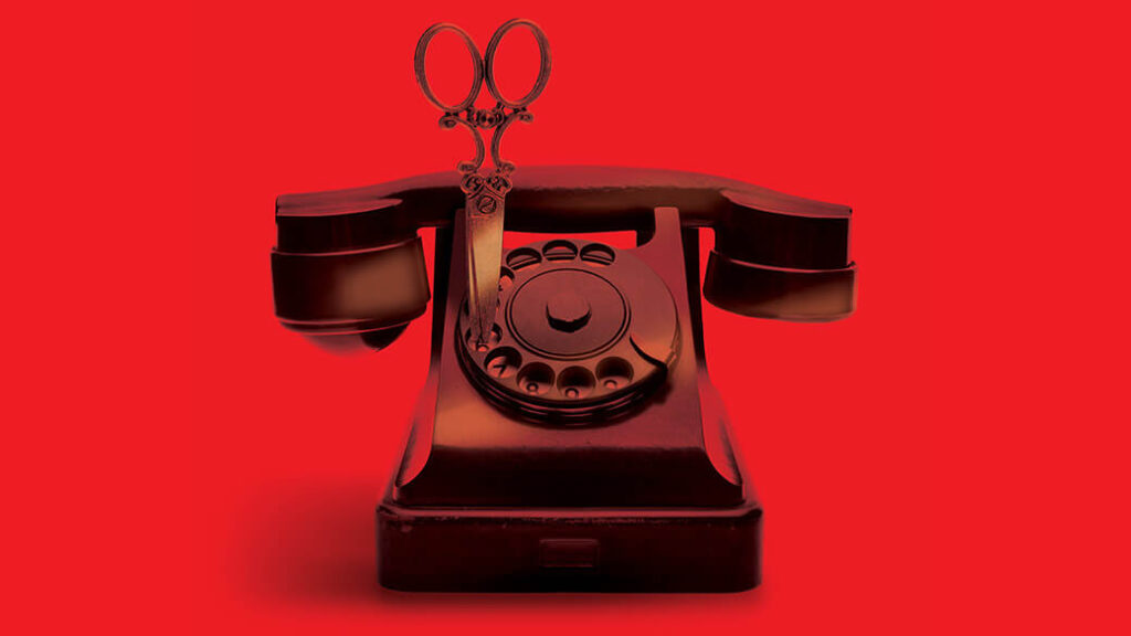 Against a deep red background is an old black dial phone with a pair of scissors stuck vertically in one of the dialing slots.