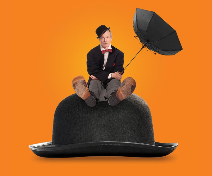 Against an orange background, a may sits on a huge bowler hat. He wears a small bowler hat, black suit, red bowtie, old shoes and holds a black blown-out umbrella.