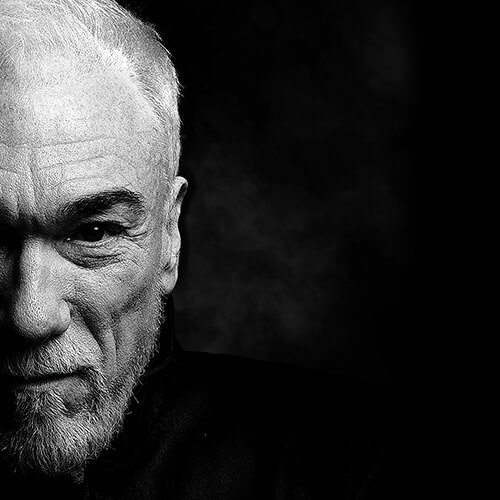 a black & white headshot of an older man with a beard on the left side of a black square