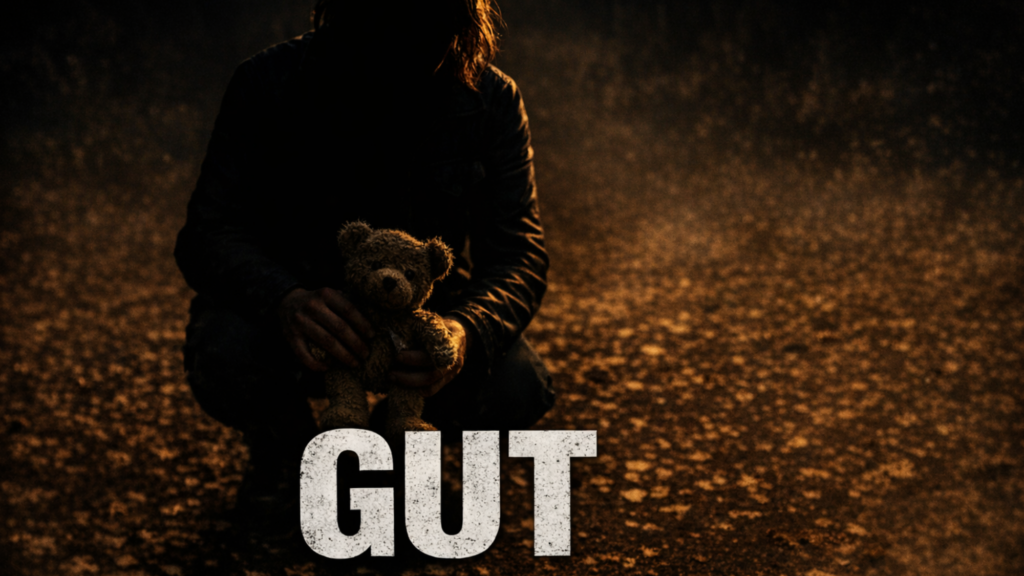 Outside A mother crouches, clutching a teddy bear in her hand. She is backlit, her features in shadow. The light coming in from the right reveals leaves on the ground.